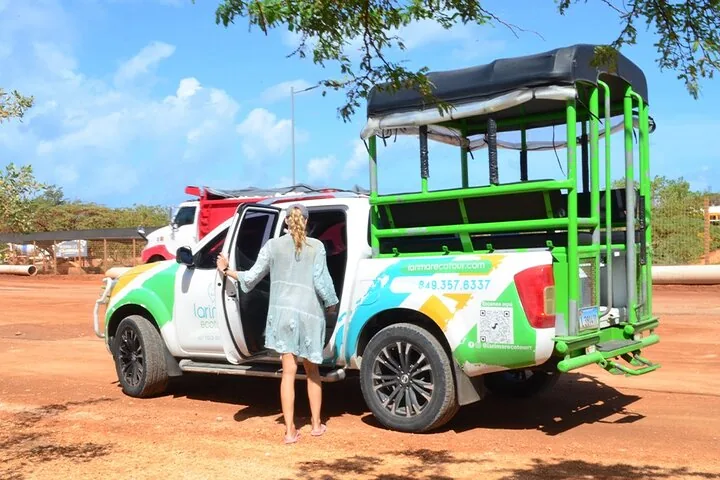 Una mujer de pie junto a un camión de excursión en un camino de tierra.