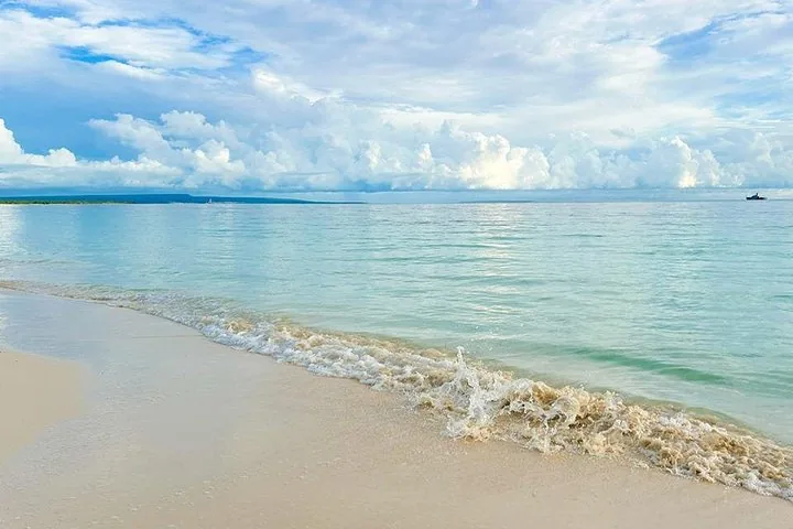 Ruhiger Strand mit weißem Sand und klarem türkisfarbenem Wasser unter bewölktem Himmel.